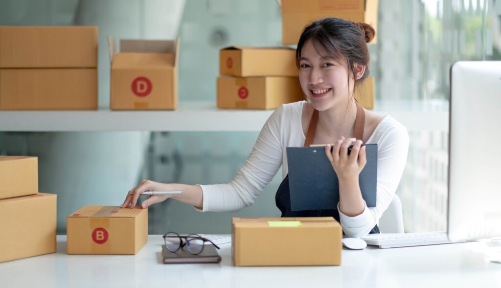Portrait young asia female owner startup look at camera work happy with box at home prepare parcel