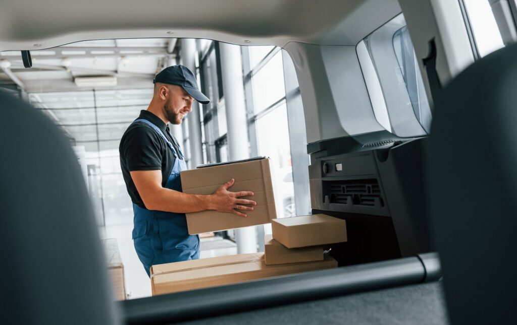 With vehicle. Delivery man in uniform is indoors with car and with order